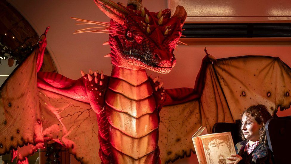 Librarian Heather Edwards reads a vintage Fairytales book by Hans Christian Andersen next to a dragon created by fantasy artist Anne Stokes