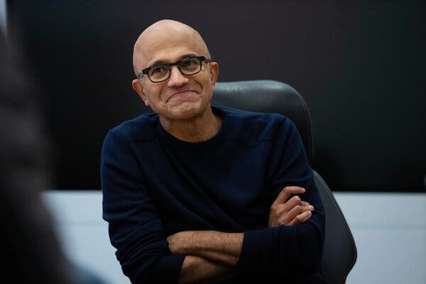 A grinning Satya Nadella sits with his arms folded. 