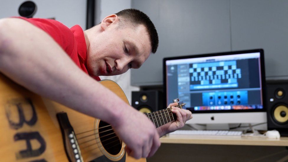 Prisoner with a guitar in front of a computer