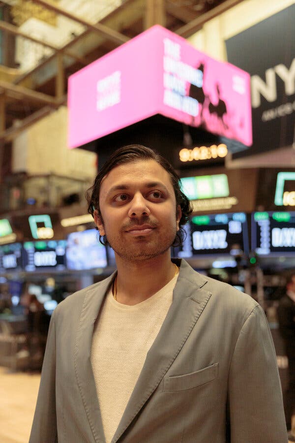 Sohail Prasad, wearing a khaki blazer and cream-colored shirt, stands on the floor of the New York Stock Exchange.