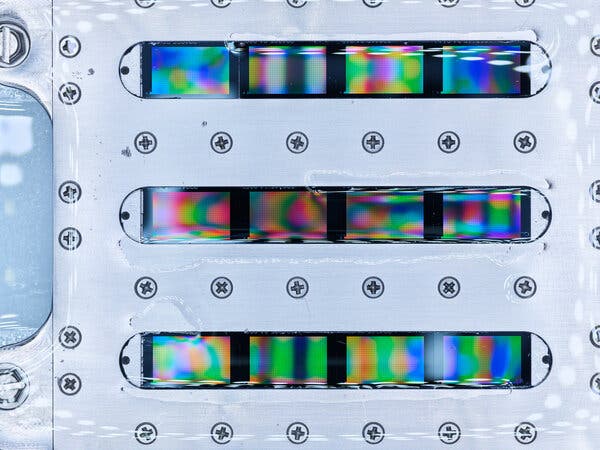 A close-up view of iridescent bands of color behind narrow horizontal windows in a metal plate. 