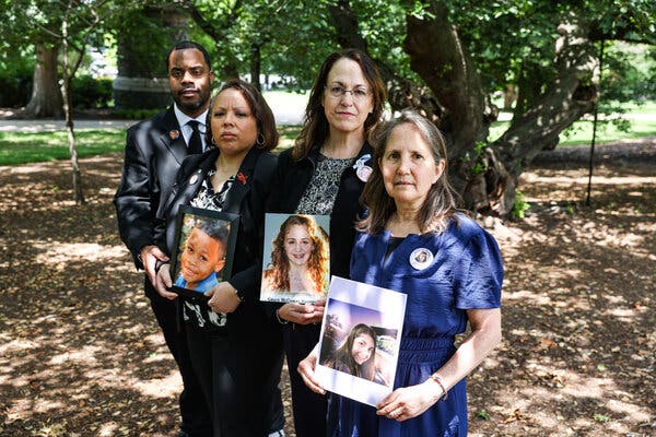 Todd and Mia Minor, Christine McComas, and Deb Schmill hold photos of their children in dappled sunlight near a tree.