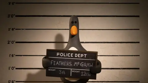 BBC Feathers McGraw appearing as if in a police line up, with a board which gives his height as three feet, and weight as 12 lb