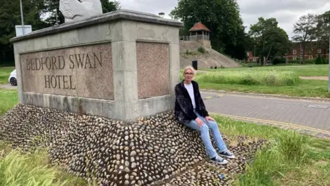 Alex Pope/BBC Ruth Hogan sitting on a hotel sign