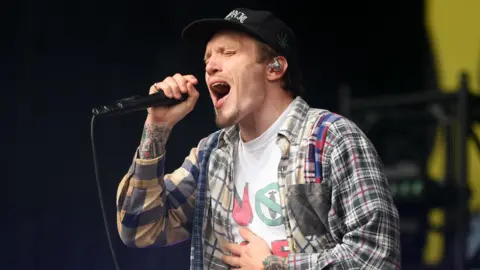 Getty Images Ben Barlow, wearing a check shirt, of Neck Deep belts into a microphone on the main stage at Leeds Festival