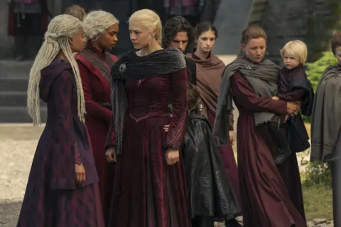 HBO House of the Dragon cast members, six women, one holding a child, all in floor length burgundy dresses