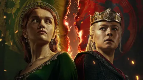 HBO Two characters from House of the Dragon with fire in the background, one woman with ginger hair wearing a green dress, another woman with blonde hair wearing chainmail dress and a crown