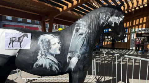 Andrew Turner/BBC Anna Sewell and Black Beauty depicted on the side of a model of a horse, being created inside Great Yarmouth Market Hall