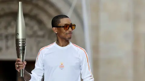 Reuters US rapper, artist and designer Pharrell Williams holds the Olympic torch as part of the 2024 Paris Olympic Games Torch Relay, on the day of the opening ceremony.