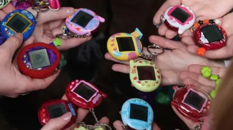 Getty Images Tamagotchi in lots of different colours. They are small egg-shaped devices with a digital screen in the middle and three buttons underneath. The colours range from a deep see-through red to bright blue, green, yellow and purple.