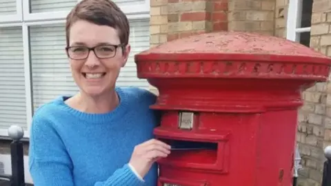 The Handwritten Letter Appreciation Society A smiling Dinah Johnson posing as she puts a letter into a postbox