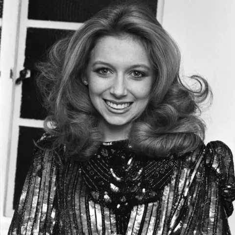 Getty Images An older Lena Zavaroni, aged 21, smiles at the camera, with a big blowout hairstyle. She is wearing a metallic sequin dress. The photo is in black and white.