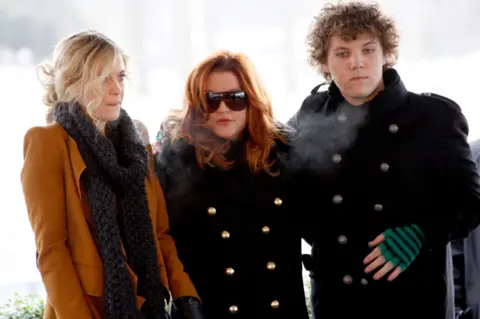 Reuters Lisa Marie Presley with her children Riley (L) and Benjamin Keough (R) at the 75th birthday celebration for Elvis Presley in Memphis, Tennessee January 2010. They all look very sombre and are wearing black, except Riley has a brown jacket on. Lisa Marie has red hair and is wearing sunglasses. Ben is in all black, but has green and black striped fingerless gloves.