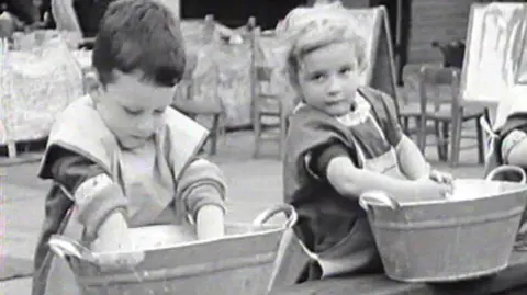 Bristol Archives A black and white photo of two young children in an outside nursery setting, playing at washing up in two large bowls