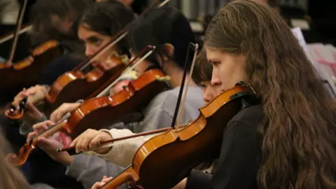 Rhian Pullen Photography A close up of a row of young musicians playing the violin in an orchestra 