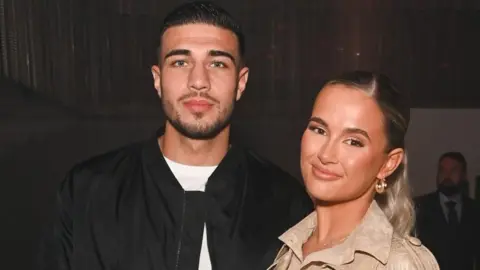 Getty Images A picture of Tommy Fury wearing black, and Molly Mae in a light coloured top against a dark backdrop