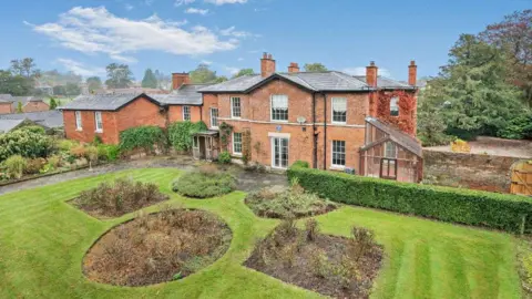 Savills A brick-built Georgian seven-bedroomed house in Oswestry with hedges, a lawn and flower beds in the foreground.