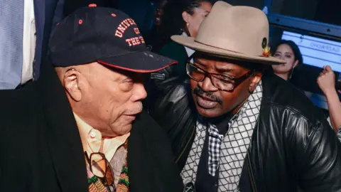 Madison McGaw/BFA.com/Shutterstock Quincy Jones Fab 5 Freddy speaking together in 2019. Jones is wearing a black baseball cap and Freddy has a beige trilby on