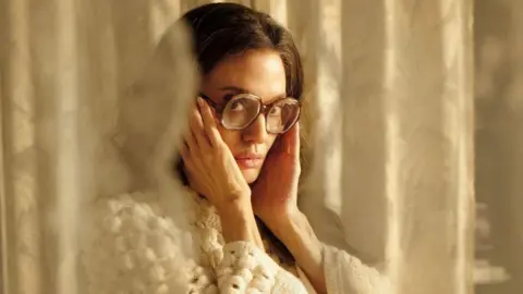 Studio Canal A picture of Angelina Jolie as Callas wearing a white sweater and large glasses