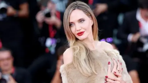 Getty Images Angelina Jolie in a faux fur dress against a backdrop of photographers 