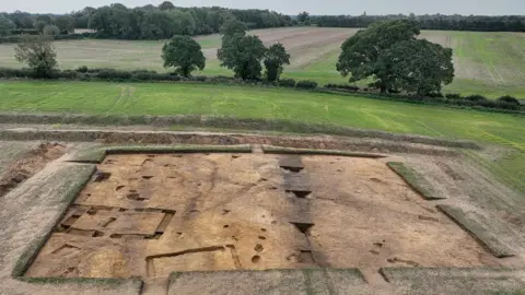 Suffolk County Council A drone image of a field that has been excavated to reveal the imprint of a large structure. Marks in the ground can be seen where the building once stood.