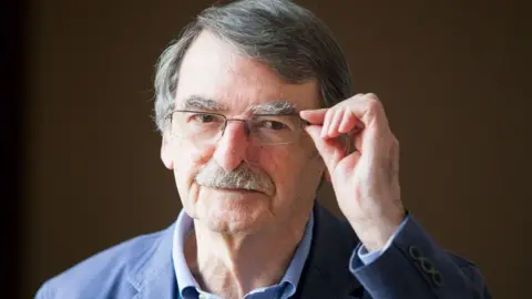 Getty Images David Lodge portrait, with him wearing a blue suit and adjusting his glasses