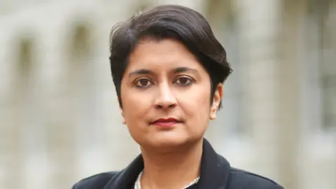 Supplied Shami Chakrabarti is looking at the camera and has short brown hair and brown eyes, and is wearing a black coat. The background behind her is blurred.