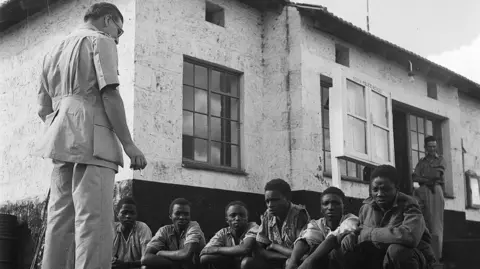 Getty Images Kikuyu tribesmen suspected of belonging to the Mau-Mau movement are interrogated by a police inspector. 1952.