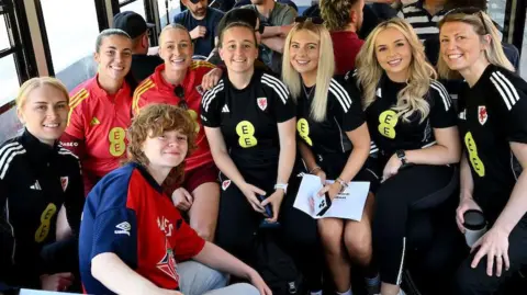 FAW A group of women dressed in black and red football kits, all looking at the camera and smiling