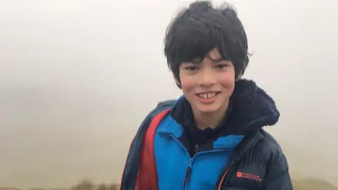 Family handout Gabriel out walking in a field with short dark hair in mist smiling at the camera.