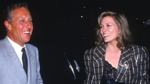 Getty Images Frederick Forsyth and Faye Dunaway attend the premiere for The Fourth Protocol. They are laughing.