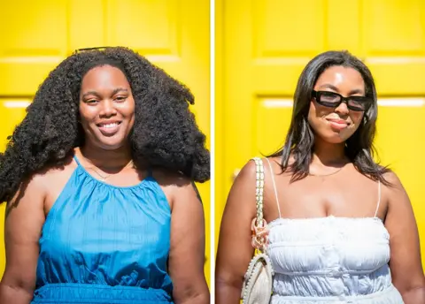 Sky and Chantelle, two young women with dark brown hair smile to the camera in front of a yellow door