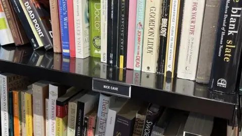 Juliette Parkin/BBC A number of the books donated by Nick Cave, on display at the Oxfam book shop in Hove, East Sussex.