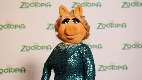 Getty Images Miss Piggy wears a sparkly green dress and has blonde hair in an up-do. 