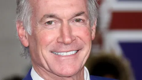 Getty Images A close-up of a man  with silver hair who is smiling at the camera.