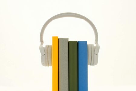 Person wearing headphones while holding books, representing the shift from physical to audio reading