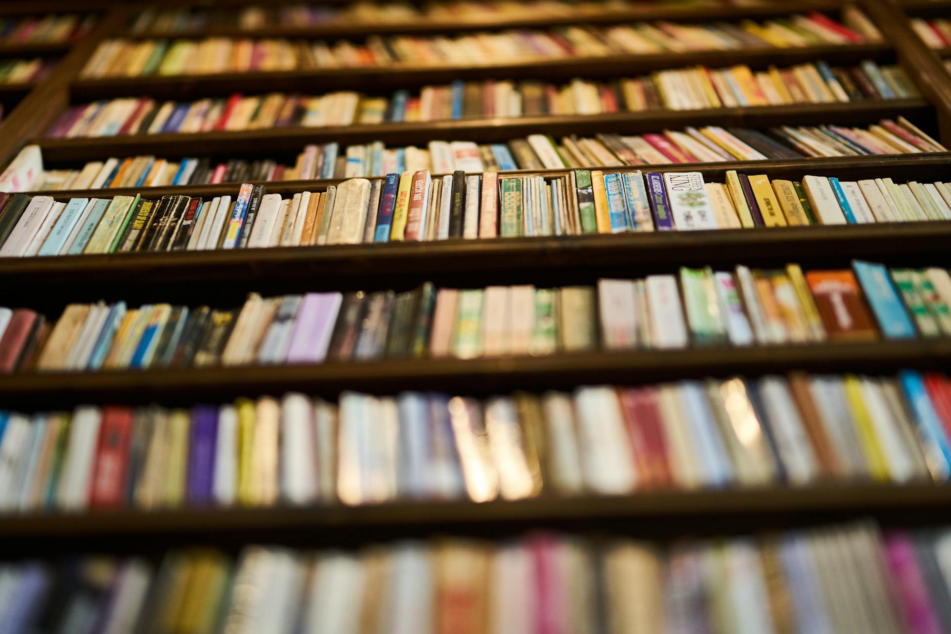 Stack of books on wooden library table with reading lamp