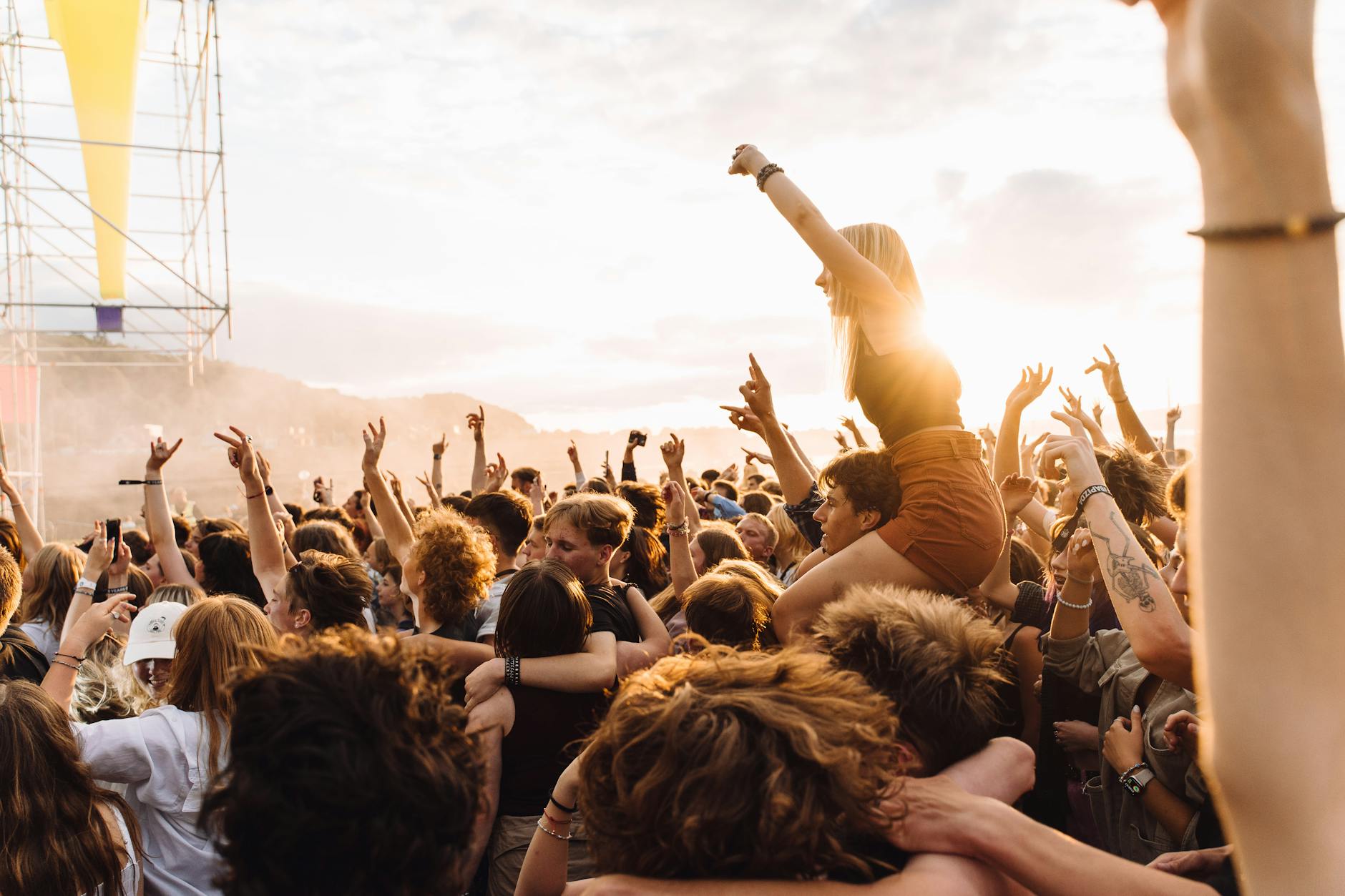 Music festival crowd silhouetted against colorful sunset sky during outdoor performance