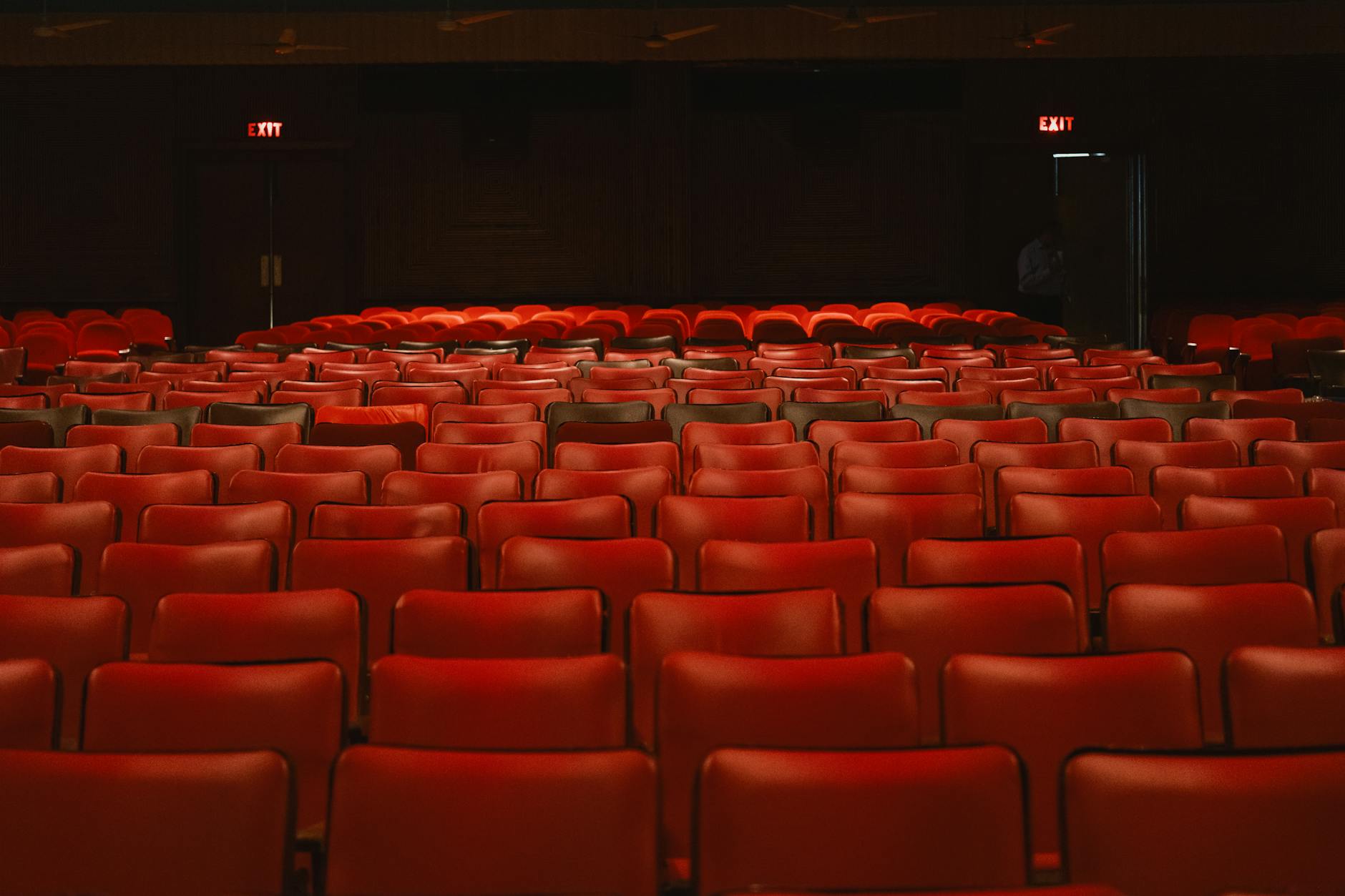 Empty red velvet theater seats in rows facing a stage