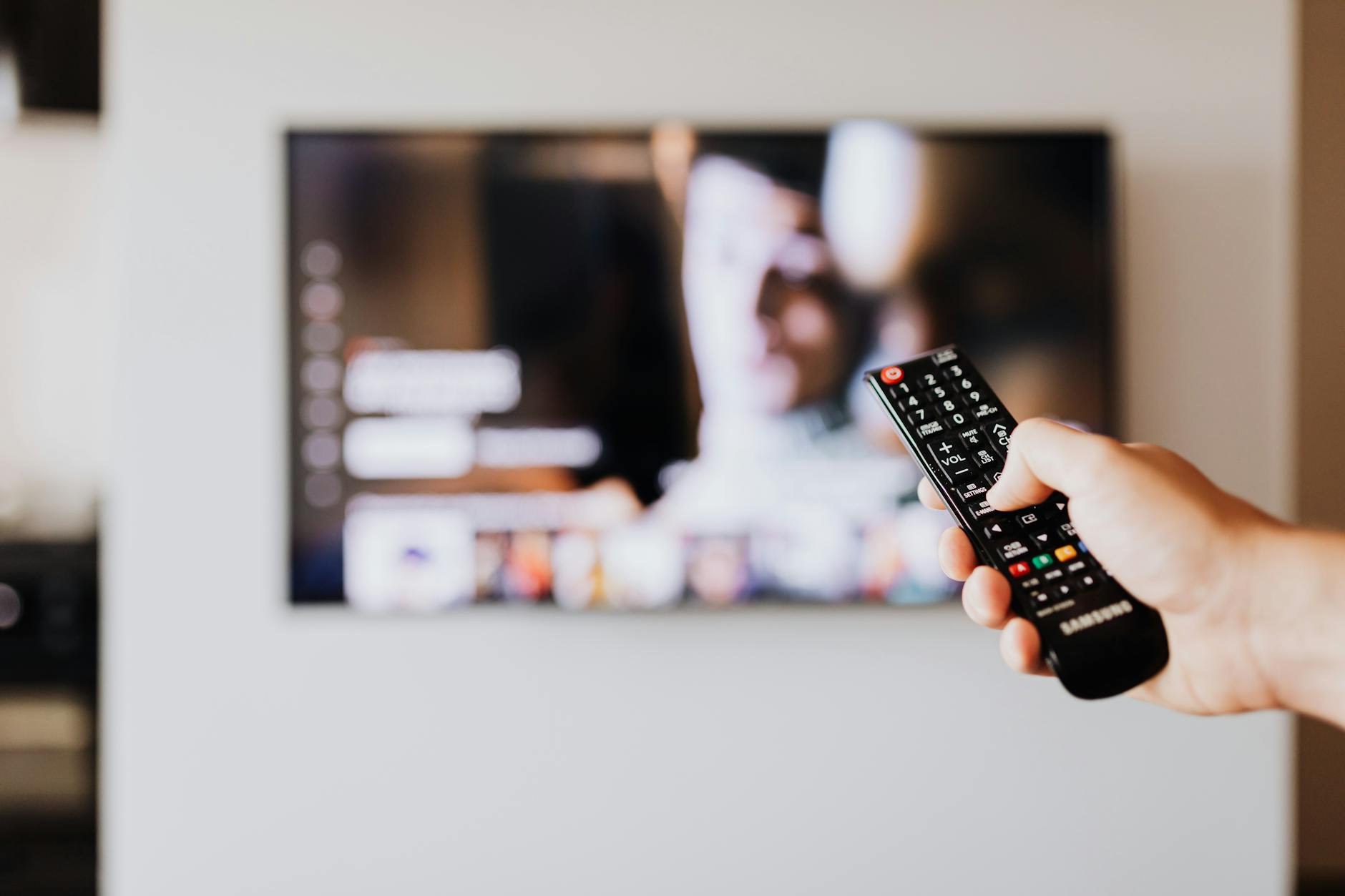Hand holding a streaming device remote control pointed toward a television screen
