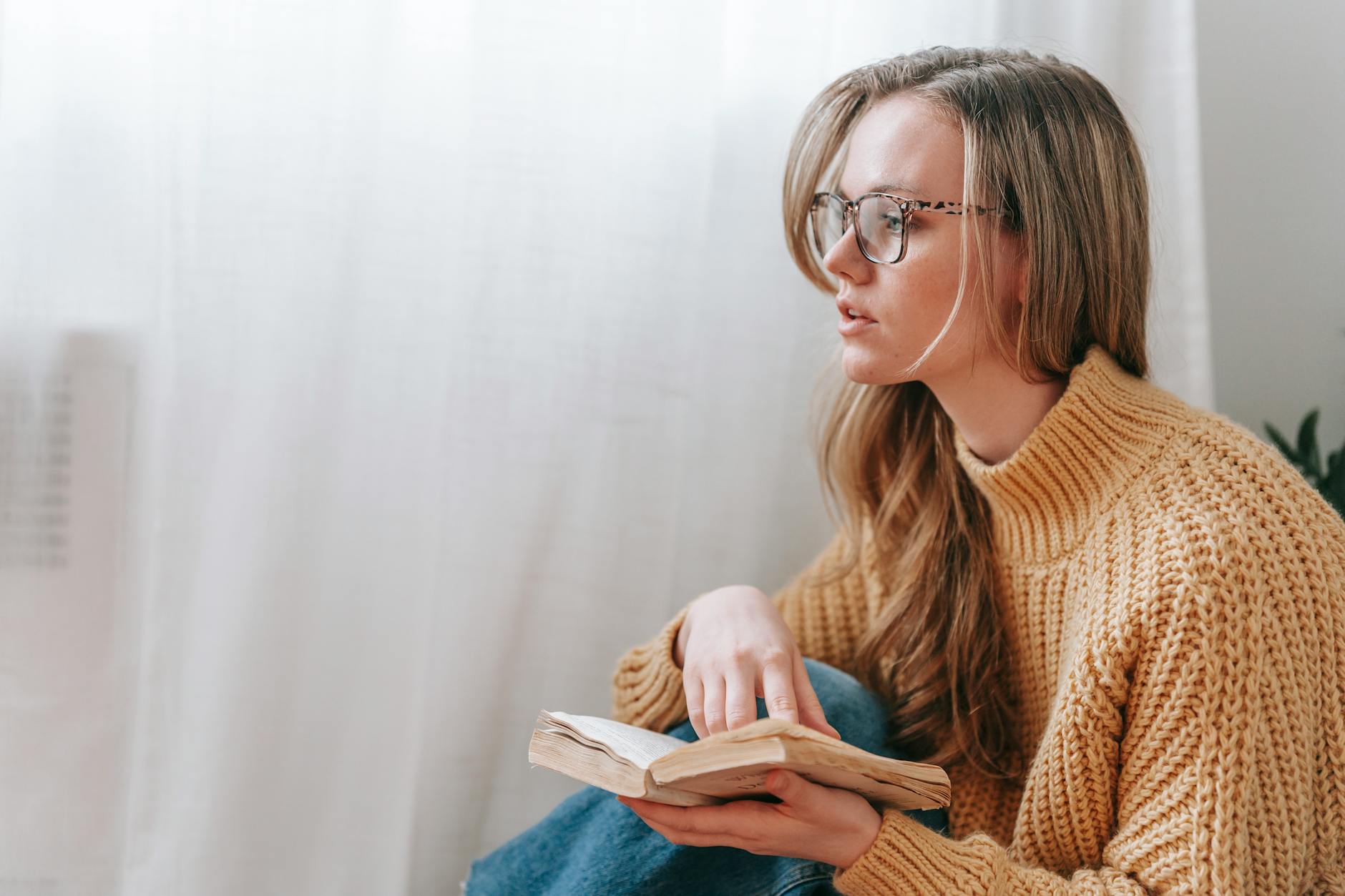 Person reading a thick book alone at a table in natural light