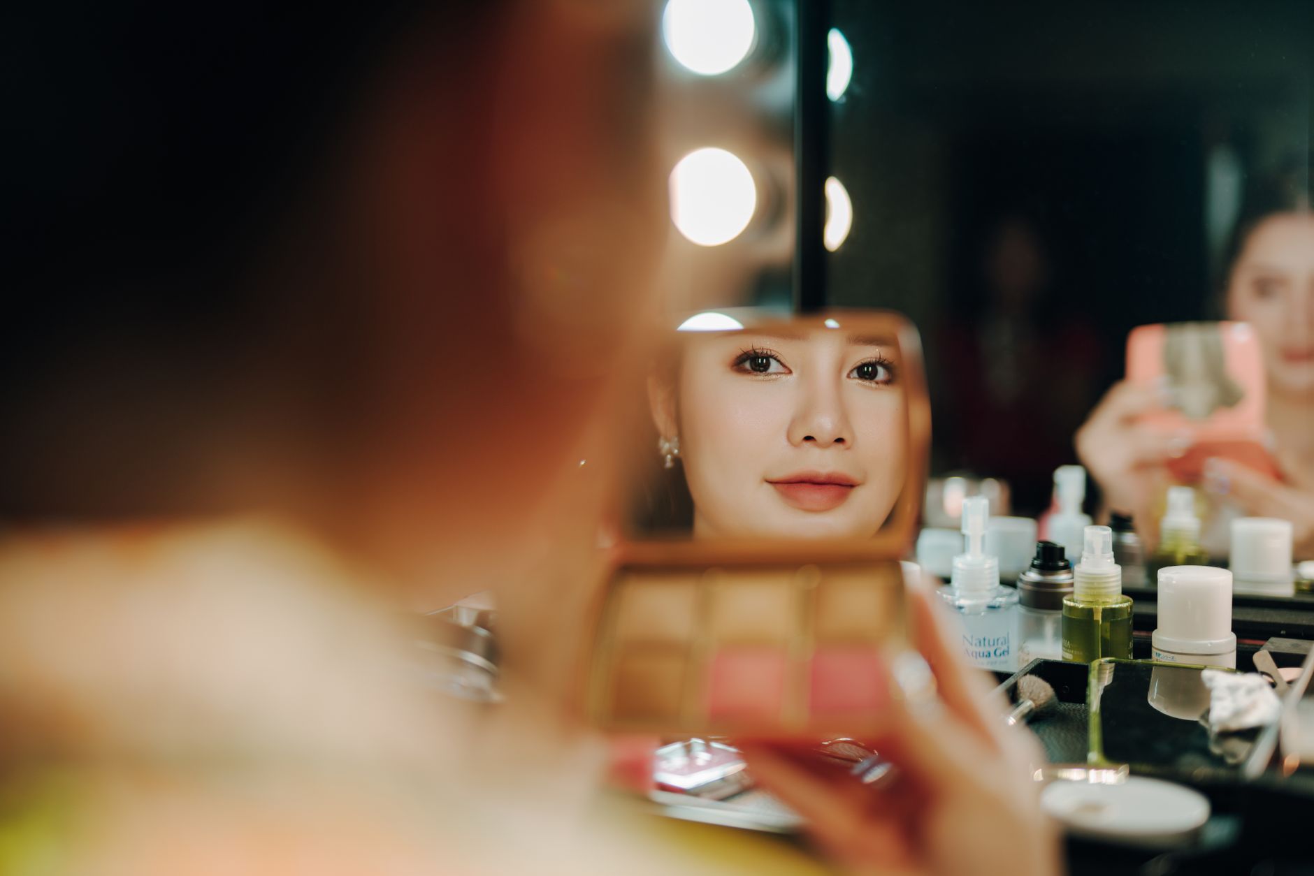 A woman sitting at a vintage vanity mirror in warm indoor lighting
