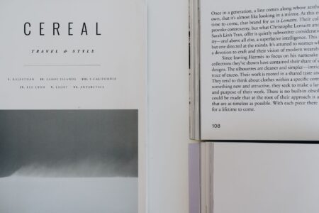 An open literary magazine resting on a wooden surface beside a cup of coffee