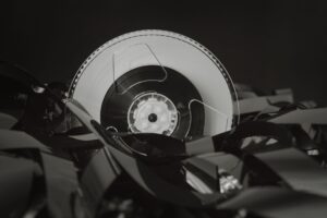 A stack of literary novels next to a vintage film reel on a wooden surface