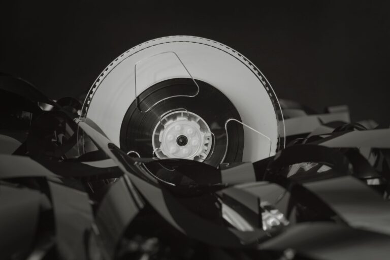 A stack of literary novels next to a vintage film reel on a wooden surface
