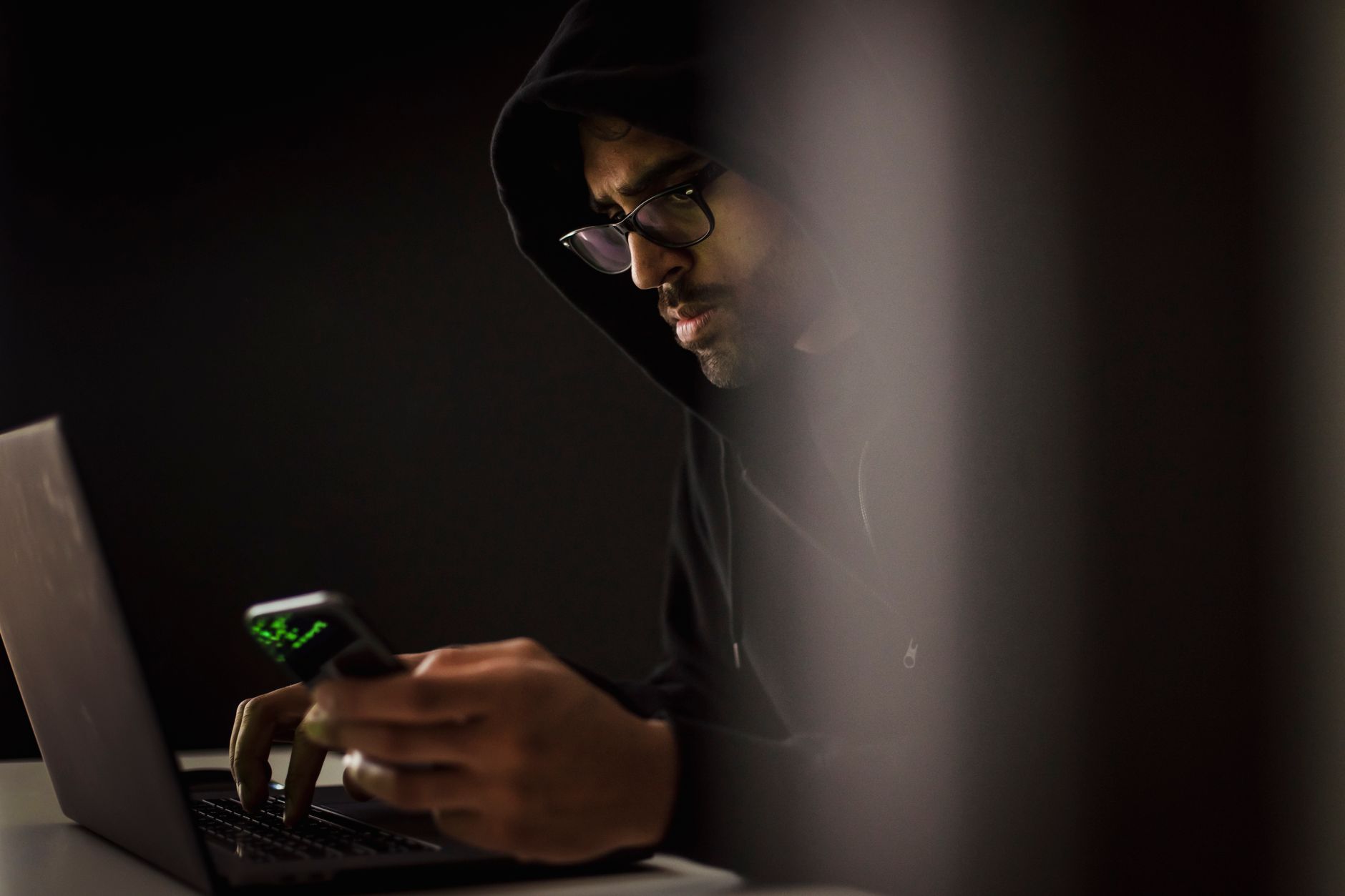 Person working on a laptop in a dark environment suggesting hacking activity