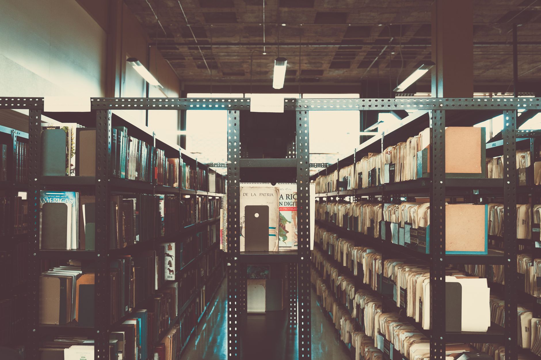 Rows of aging books on wooden library shelves, suggesting publishing history
