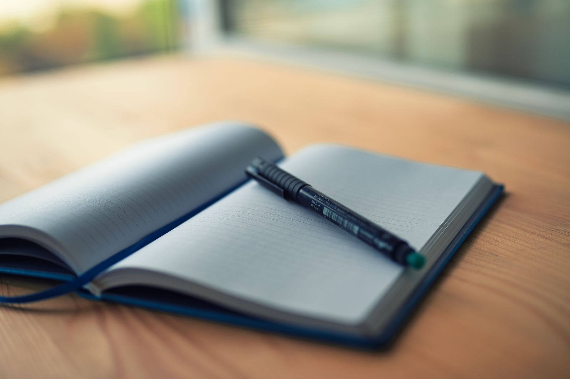 Writer's notebook and pen resting on a wooden desk beside a lamp