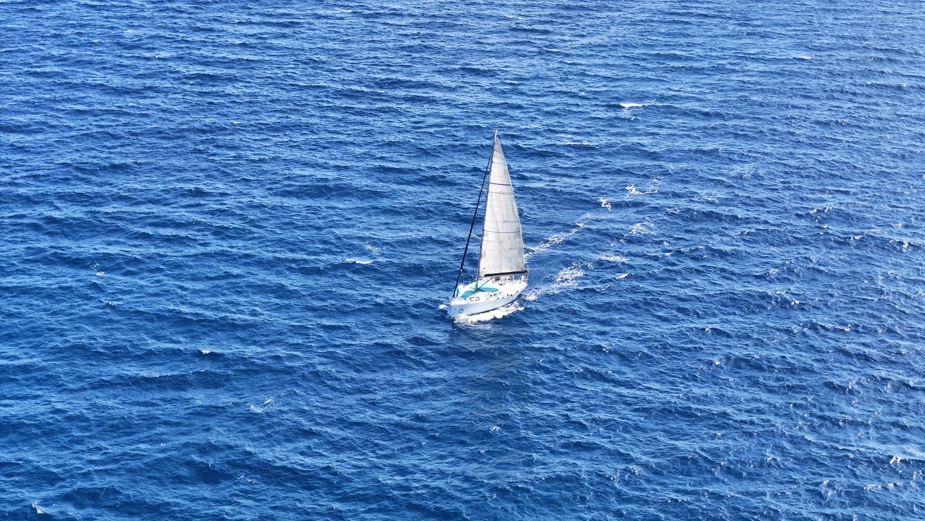 Small sailing vessel crossing open ocean under overcast sky
