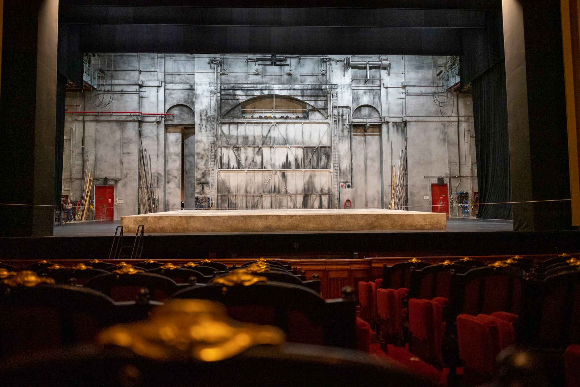 A dramatic red curtain on an empty theater stage, referencing Phantom of the Opera debates